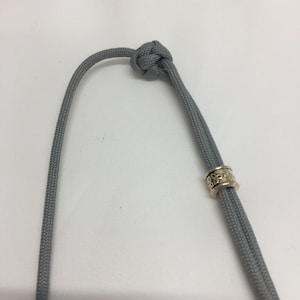 May include: A gray paracord bracelet with a gold bead featuring a Celtic knot design.