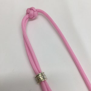 May include: A pink paracord lanyard with a silver bead. The lanyard has a knot at the top.