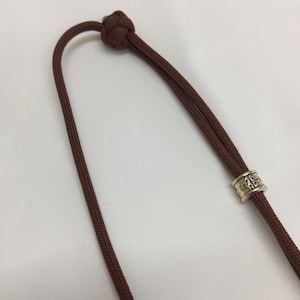 May include: A brown cord necklace with a silver bead featuring a Celtic knot design.