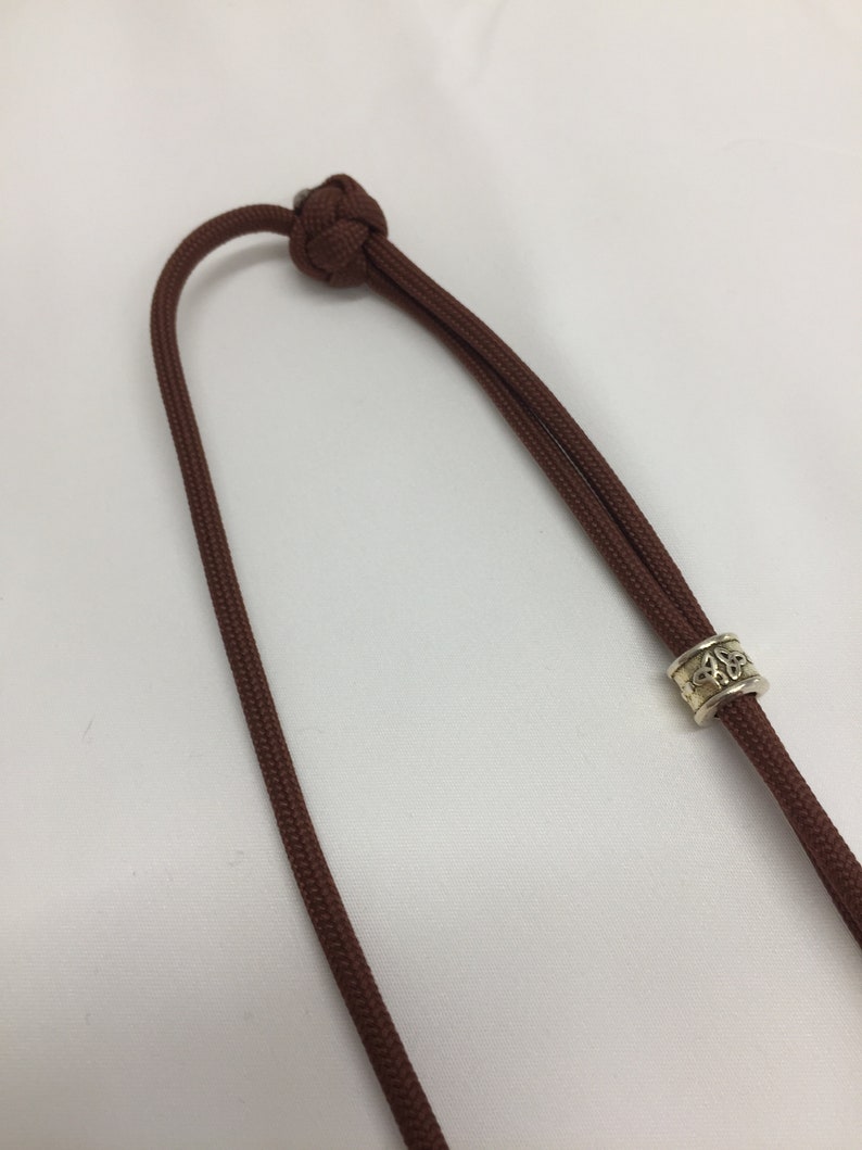 May include: A brown cord necklace with a silver bead featuring a Celtic knot design.