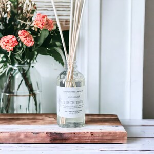 May include: A clear glass bottle with a white label that reads "London James Candle Co. Reed Diffuser Birch Tree Eucalyptus, mint, cypress, pine, cedar smoke, patchouli & vetiver 4 oz. Made in Lexington, South Carolina"