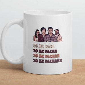 May include: White ceramic mug featuring a cartoon illustration of four people. Below the illustration, the text reads "TO BE FAIR" repeated four times with varying numbers of "R"s. The mug has a curved handle and is set on a wooden surface.