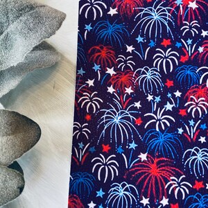 May include: A dark blue background is covered with a pattern of white, red, and blue fireworks and stars. The fireworks are stylized with white outlines and red and blue accents. The design is reminiscent of a patriotic theme.