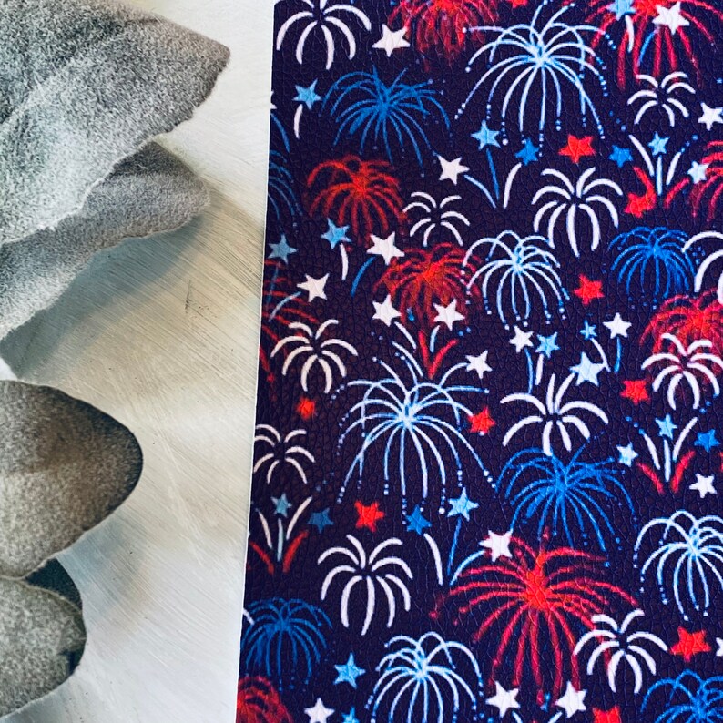 May include: A dark blue background is covered with a pattern of white, red, and blue fireworks and stars. The fireworks are stylized with white outlines and red and blue accents. The design is reminiscent of a patriotic theme.