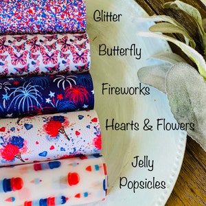 May include: A stack of patterned faux leather rolls. Designs include glitter, butterflies, fireworks, hearts and flowers, and jelly popsicles. The color scheme is red, white, and blue.