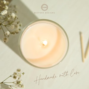 May include: Overhead view of a lit candle in a clear glass container. The candle has a soft, peach-colored wax and a single wick. The text "Handmade with Love" is written in cursive. The words "L&M Bespoke Designs" are also visible.