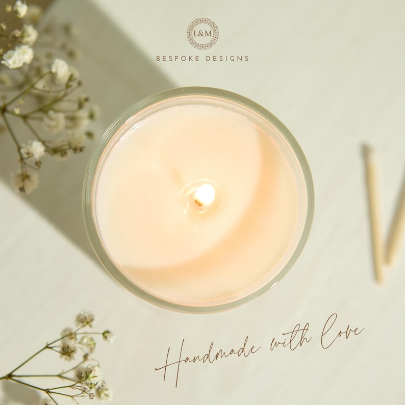 May include: Overhead view of a lit candle in a clear glass container. The candle has a soft, peach-colored wax and a single wick. The text "Handmade with Love" is written in cursive. The words "L&M Bespoke Designs" are also visible.