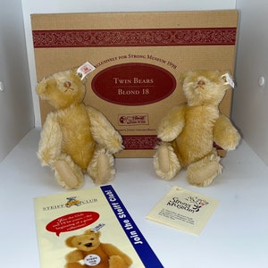 May include: Two light brown Steiff teddy bears, each with a button in their ear, sitting on a brown box with the text "Exclusively for Strong Museum 1998" and "Twin Bears Blond 18".