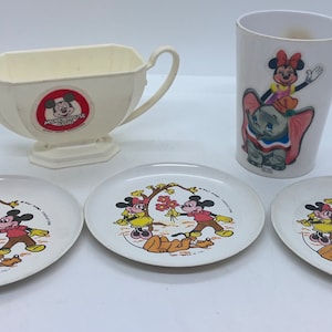 Könnte beinhalten: Ein Vintage-Kinder-Tee-Set von Mickey Mouse mit einer weißen Sauciere, drei weißen Tellern mit Mickey Mouse und Minnie Mouse Illustrationen und einer weißen Tasse mit Mickey Mouse, der auf Dumbo dem Elefanten reitet. Die Sauciere hat einen roten Aufkleber mit dem Text "Mickey Mouse Clubhouse".