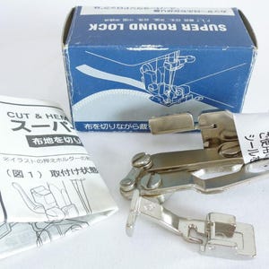 Pode incluir: Um acessório para máquina de costura Super Round Lock, com uma caixa azul e um manual de instruções. O acessório é de metal prateado. A caixa tem texto japonês e uma ilustração do acessório em uso. O manual também tem texto e diagramas japoneses.