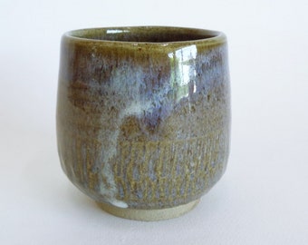 Peut inclure: Une tasse en céramique brune avec un glaçage blanc et bleu. La tasse a une surface texturée et un fond arrondi.