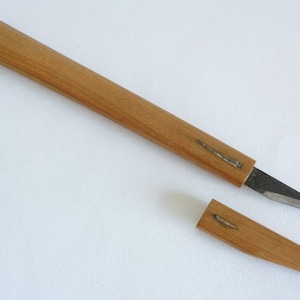 May include: A wooden knife handle with a metal blade. The handle is made of light brown wood and has a metal inlay. The blade is thin and sharp. The knife is separated from the handle, showing the two pieces.
