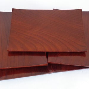 Puede incluir: Un conjunto de cuatro platos rectangulares de madera en un tono marrón rojizo oscuro. Los platos tienen una superficie brillante y un borde ligeramente curvado. La veta de la madera es visible.