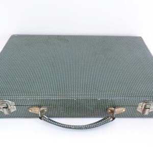 May include: A vintage, rectangular suitcase with a teal and white polka dot pattern. The suitcase has metal latches and a handle. The case is closed and sits on a white surface.