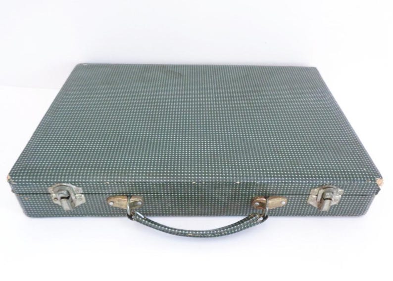 May include: A vintage, rectangular suitcase with a teal and white polka dot pattern. The suitcase has metal latches and a handle. The case is closed and sits on a white surface.
