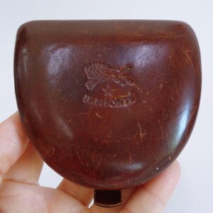 May include: A dark brown leather coin purse with a rounded, semi-circular shape. The surface features a debossed logo of a bison above a star and the text IL BISONTE. The leather has a smooth, polished finish with visible natural grain textures.