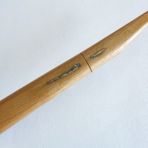Op de afbeelding: Een houten schede voor een Japans zwaard, bekend als een saya. De saya is gemaakt van lichtbruin hout en heeft een lichte kromming. Er zijn twee dunne, zilverkleurige metalen accenten op de saya.