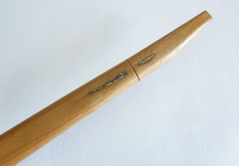 Op de afbeelding: Een houten schede voor een Japans zwaard, bekend als een saya. De saya is gemaakt van lichtbruin hout en heeft een lichte kromming. Er zijn twee dunne, zilverkleurige metalen accenten op de saya.
