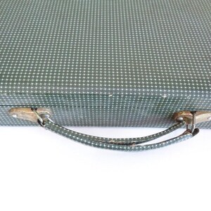 May include: Vintage green suitcase with a white dotted pattern. The suitcase has a metal clasp and handle. The handle is green with a white dotted pattern. The suitcase is on a white background.