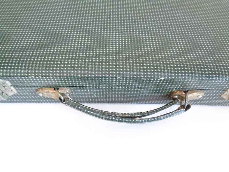May include: Vintage green suitcase with a white dotted pattern. The suitcase has a metal clasp and handle. The handle is green with a white dotted pattern. The suitcase is on a white background.