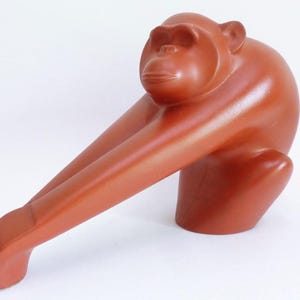 Könnte beinhalten: Eine Terrakotta-Skulptur eines Affen, der auf seinen Hinterbeinen sitzt und die Arme ausgestreckt hat. Der Affe ist aus glattem, rotbraunem Ton gefertigt.