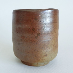 Puede incluir: Una taza de cerámica cilíndrica hecha a mano, con una estética rústica y terrosa. La taza presenta un degradado de tonos marrones, que van de un tono más oscuro en la parte superior a un tono beige más claro en la base. La superficie tiene una textura.