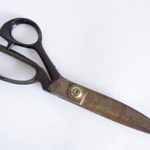 Puede incluir: Tijeras de sastre vintage con mangos negros y una hoja deslustrada de color plateado. Las tijeras tienen un lazo grande para el pulgar y otro más grande para varios dedos. Las hojas miden aproximadamente 20 cm de largo.