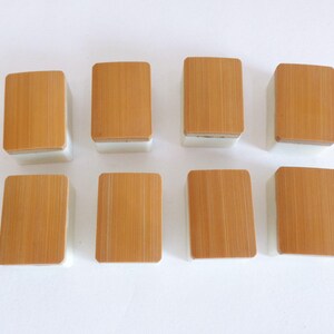 May include: Eight rectangular mahjong tiles. Each tile has a light brown, bamboo-like top and a white base. The tiles are arranged in two rows of four, with the tops facing upwards. The bamboo grain is visible on each tile.