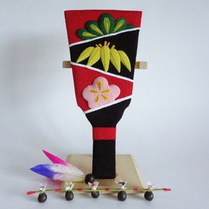 Puede incluir: Un abanico de madera tradicional japonés pintado a mano con paneles de tela roja, negra y blanca decorados con diseños florales verdes y amarillos. El abanico está montado en un soporte de madera con una pequeña clavija de madera y una cadena de cuentas negras.