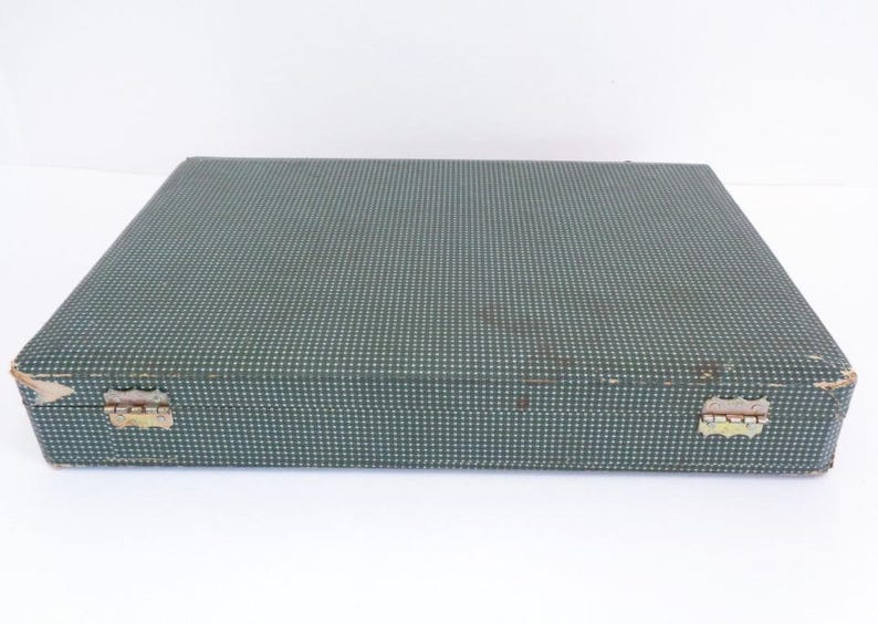 May include: A rectangular, vintage case with a teal and white polka dot pattern. The case has metal hinges and a clasp. The corners show signs of wear. The case is likely for storing flatware or other items.