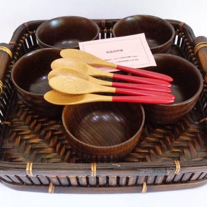 May include: A set of six brown wooden bowls with red and wooden spoons, all arranged in a woven brown bamboo tray.