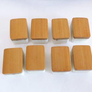 May include: Eight rectangular containers with light brown bamboo lids and white bases are arranged on a white surface. The lids have a natural wood grain, and the containers are evenly spaced.