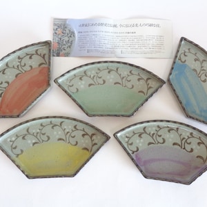 Puede incluir: Conjunto de cinco platos de cerámica en forma de abanico con un esmalte verde y un diseño floral marrón. Cada plato tiene un acento de color diferente: naranja, verde, azul, amarillo y morado.