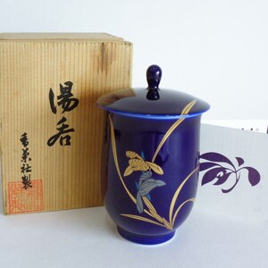 Puede incluir: Una taza de té de cerámica azul con tapa, decorada con diseños florales dorados y azules. La taza de té está en una caja de madera con caracteres japoneses que dicen "壽喜" y "香月社製".