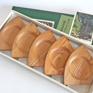 May include: Set of five wooden coasters in a white box. The coasters are shaped like a leaf and have a natural wood finish. The box has a green lid with a Japanese postcard on top.