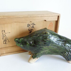 May include: A green ceramic boar figurine with a wooden box. The box has Japanese writing on it.