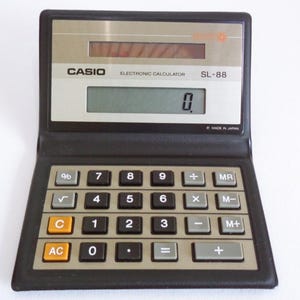 May include: A black and silver Casio SL-88 electronic calculator with a digital display and a full set of buttons. The calculator has a black plastic case and a silver faceplate with the Casio logo and model number.