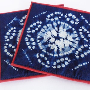 May include: Two blue and white tie-dye fabric coasters with red edging.