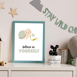 May include: A teal framed print with a white background featuring a cartoon turtle holding a dandelion with the text "believe in YOURSELF" in black and green.