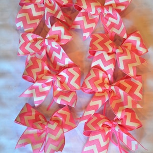 Op de afbeelding: Een verzameling roze en witte haarstrikken met chevron-patroon. De strikken zijn in een rij op een wit oppervlak gerangschikt.