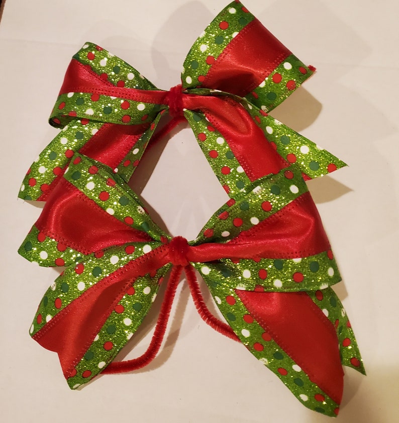 May include: Two red and green Christmas bows with white polka dots and glitter. The bows are tied together with a red velvet ribbon.