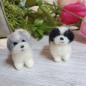 May include: Two needle felted Shih Tzu dogs. One dog is white with gray fur on its head and the other dog is white with black fur on its head.