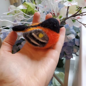 May include: A hand-felted orange, black, and yellow bird with a black head and a yellow spot on its chest.
