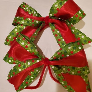 May include: Two red and green Christmas bows with white polka dots and glitter. The bows are tied together with a brown pipe cleaner.
