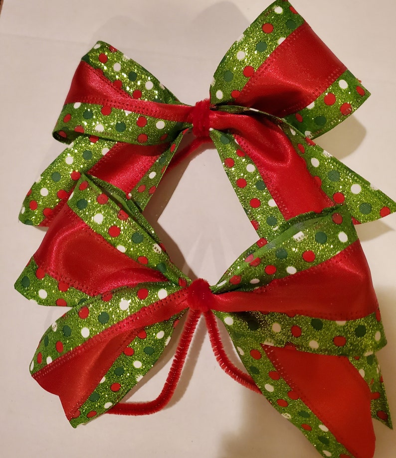 May include: Two red and green Christmas bows with white polka dots and glitter. The bows are tied together with a brown pipe cleaner.