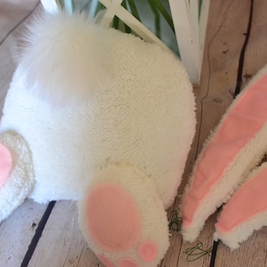 May include: White plush bunny costume with pink felt accents. The costume includes a tail, two ears, and two feet.