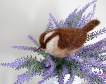 May include: A brown and white needle felted bird perched on a bouquet of purple lavender flowers.