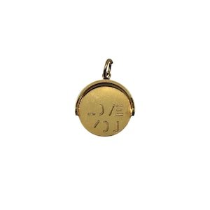 May include: A circular gold pendant featuring a rotating center disc with engraved abstract markings. The pendant is suspended from a small gold jump ring at the top, showcasing a polished metallic finish and a mechanical design that allows the central circular component to spin freely within its frame.
