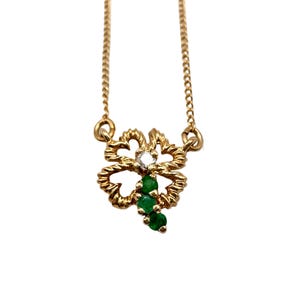 Op de afbeelding: Een goudkleurige ketting met een klaverblad hanger. De klaver heeft een centrale diamant en drie groene smaragden. De ketting is fijn en de hanger is gedetailleerd.