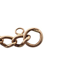 May include: Close-up of a gold-colored chain clasp. The clasp is made of interlocking oval links and a circular ring. The metal has a warm, polished finish. The clasp is set against a white background.